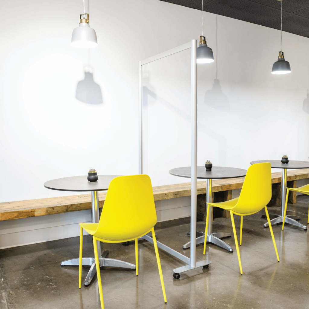 Loftwall clear acrylic Split privacy screen in between yellow cafe chairs in break room
